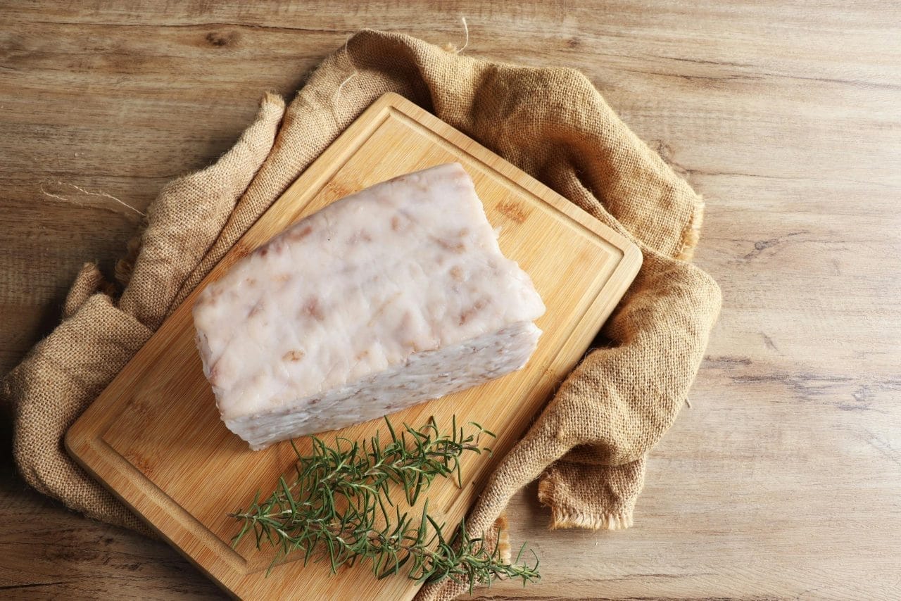 Top view of pork fatback block with rosemary on a wooden chopping board. Perfect for culinary ingredients display.