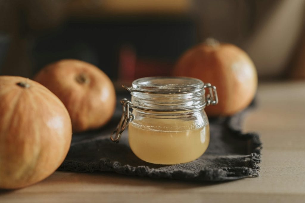 A cozy still life with homemade apple cider in a glass jar surrounded by pumpkins on a wooden table.