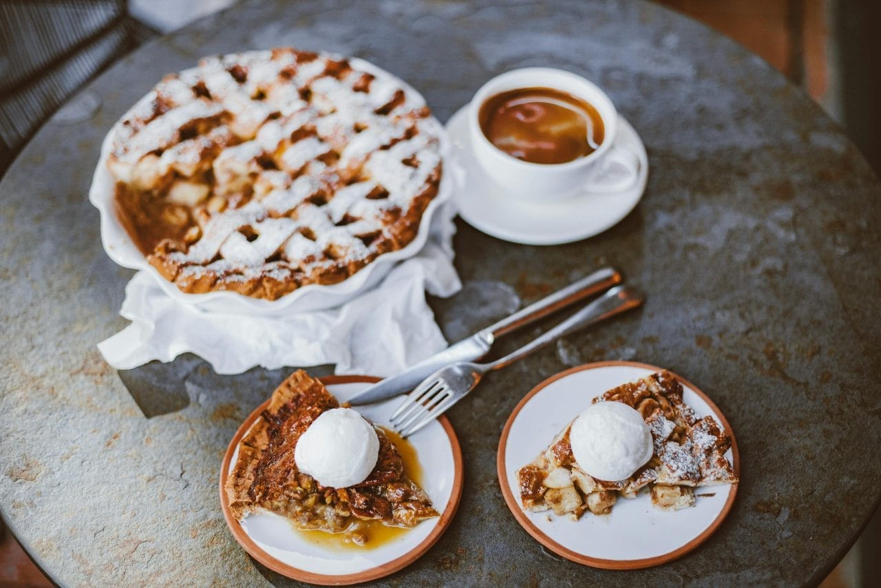 A mouthwatering apple pie with ice cream serving alongside tea on a cozy table setup.