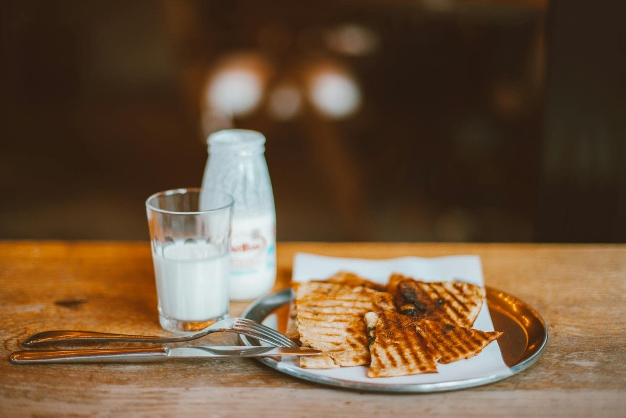 A warm breakfast setting with grilled tortilla, milk bottle, and cutlery on a rustic table.