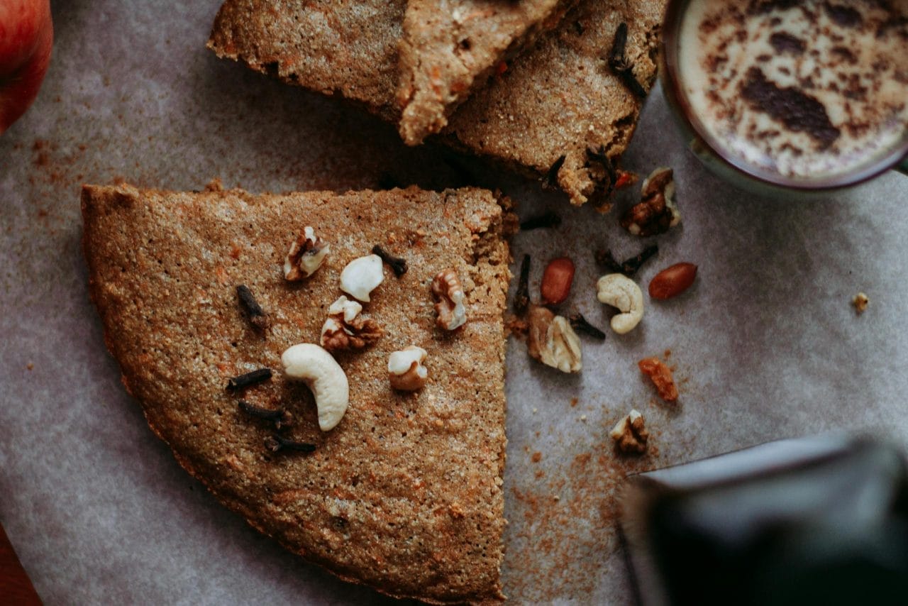Top view of a homemade carrot cake with nuts next to a cup of coffee.